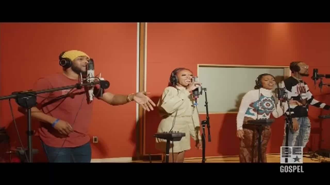 Four singers, each with a microphone, stand in a recording studio, all facing forward. The man in the red shirt gestures with his right hand as the others sing, clearly in the middle of a performance for BET Gospel.
