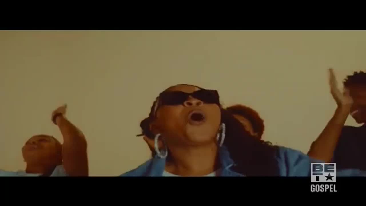 A woman in sunglasses belts out a song, her mouth wide open, while others around her raise their hands. The BET Gospel logo is in the corner, and it looks like a music video.

