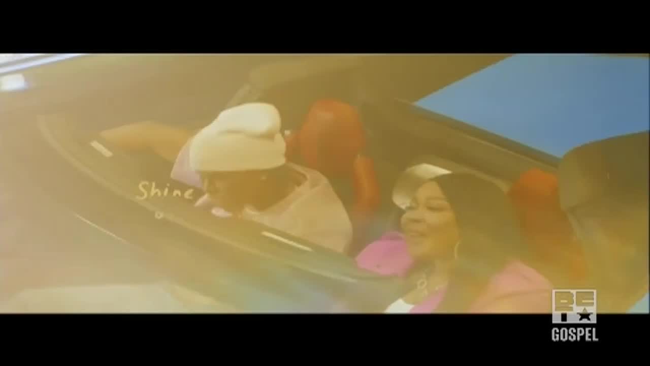 A woman in a pink top smiles from the passenger seat of a car.  The "BET Gospel" logo is in the corner as the car moves.
