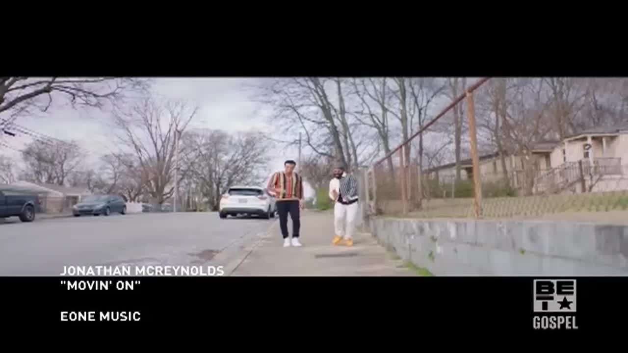 Two men, dressed in casual clothes, walk down a residential street. The scene is a music video for BET Gospel, with the artist's name and song title displayed at the bottom.
