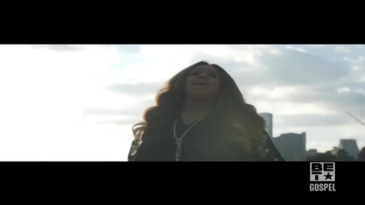 A woman with long, wavy hair is singing, her face tilted toward the sky. The BET Gospel logo sits in the corner, and a city skyline is visible in the background.
