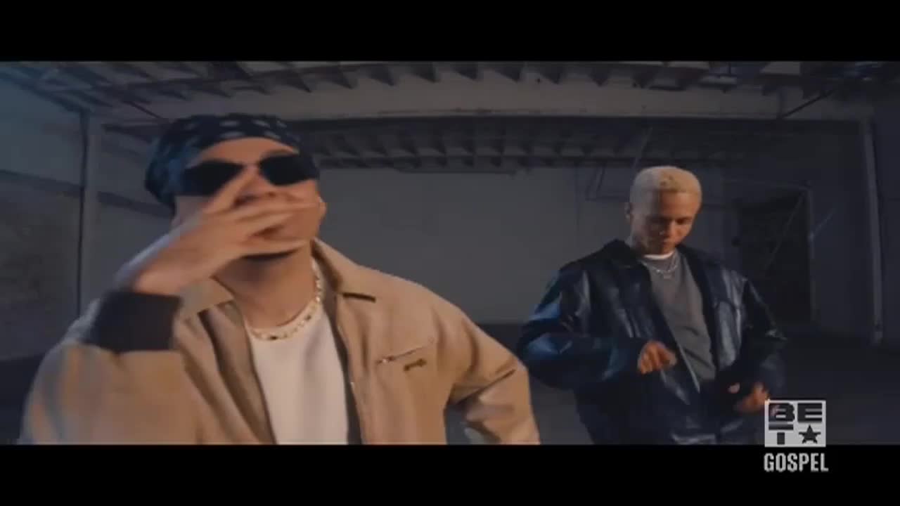 The man in the bandana covers his mouth with his hand, while the other man in the leather jacket stands nearby. It looks like they're filming a music video for BET Gospel.
