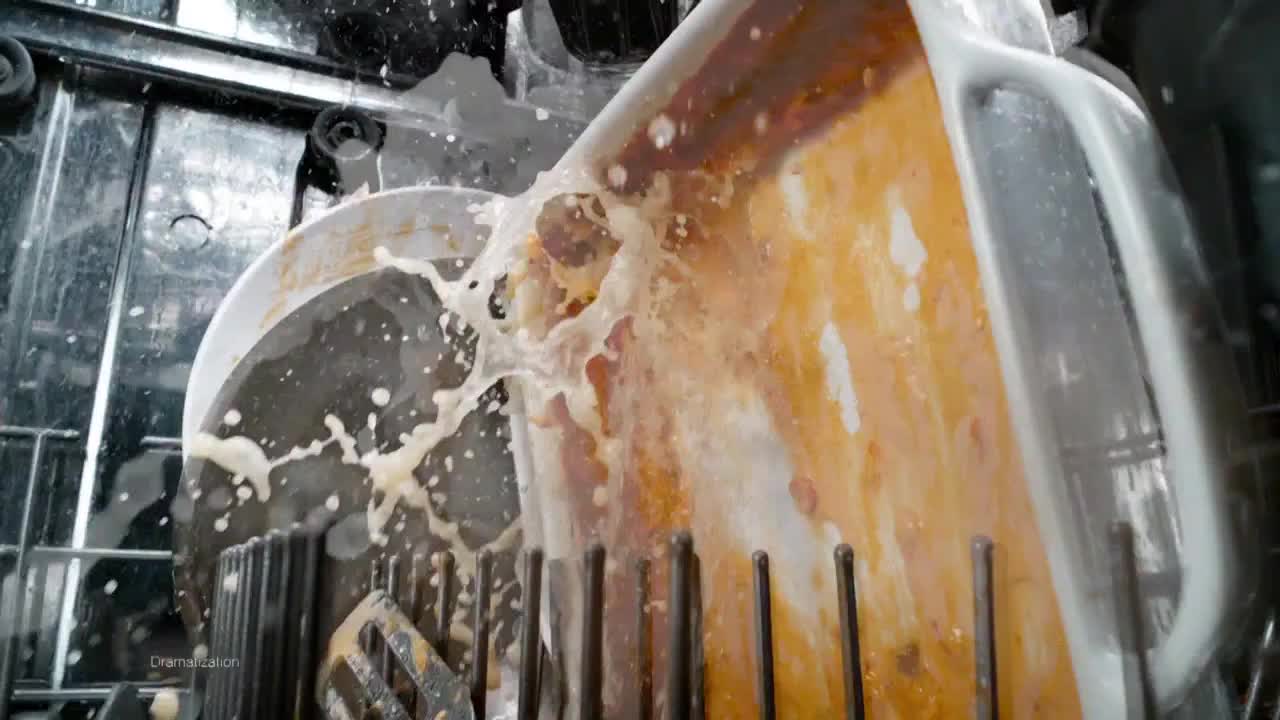 A powerful stream of soapy water blasts a dirty baking pan in a dishwasher. The spray explodes outward, creating a foamy, milky cloud.
