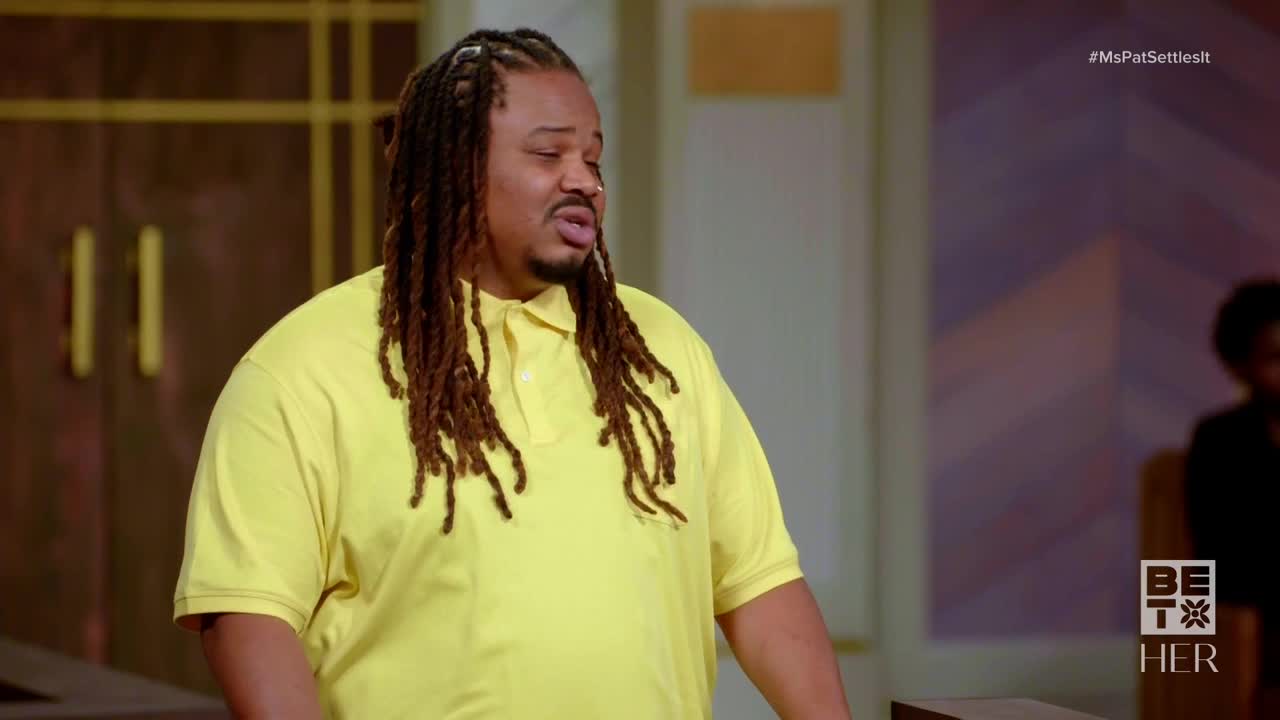 A man in a yellow polo shirt, with long dreadlocks, is speaking with his mouth open. He appears to be on a set for BET Her's *Ms. Pat Settles It*.
