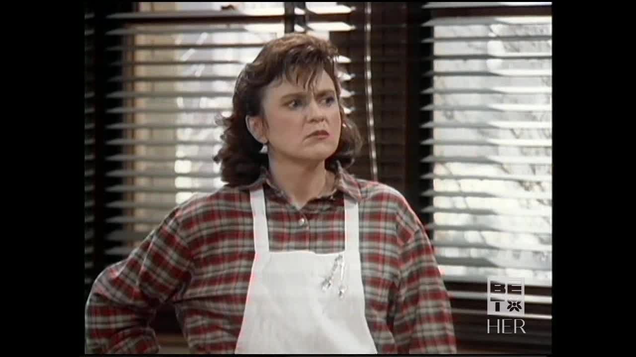A woman in a plaid shirt and white apron stands, her face set in a frown. The BET Her logo is visible in the corner.
