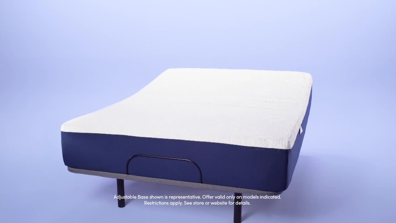 A white mattress sits atop a dark blue base, elevated slightly. The bed frame is a simple metal design, with a blue background.
