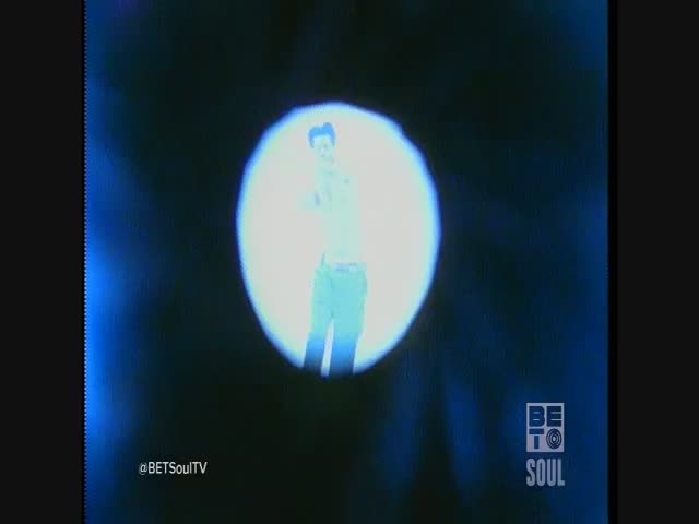 A figure, illuminated in a bright spotlight, stands center stage. The silhouette of a man is visible against the glowing backdrop.
