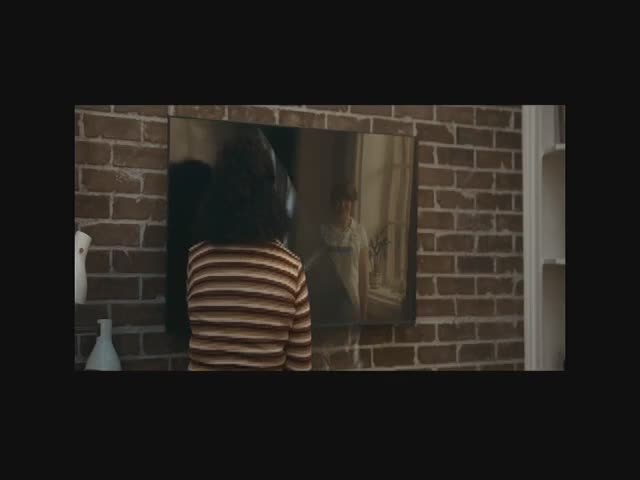 A person in a striped shirt stands facing a mirror, their dark hair obscuring their face. The mirror reflects a room with a window, as if from a scene on BET Soul.
