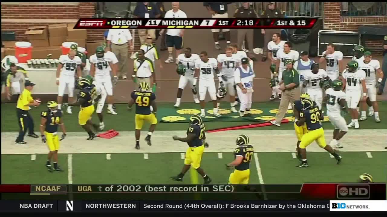 The Michigan players in their yellow and blue uniforms are celebrating, some are jumping. The Oregon team stands on the sidelines, watching the play unfold.
