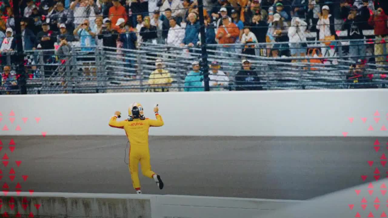 A driver in a yellow suit is running towards the crowd, arms raised in celebration. The stands are packed with fans, and the Big Ten Network logo is visible in the corner.
