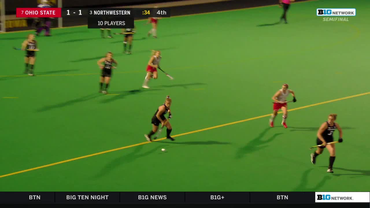 The Ohio State and Northwestern field hockey teams are battling in the fourth quarter. A player in black sprints toward the ball, while another in red chases after her.
