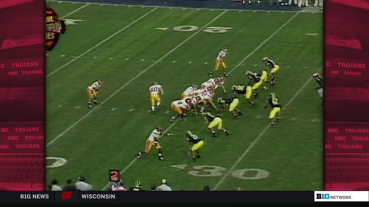The Trojans are huddled, poised to snap the ball. Players in yellow and black jerseys are spread out, ready to react.
