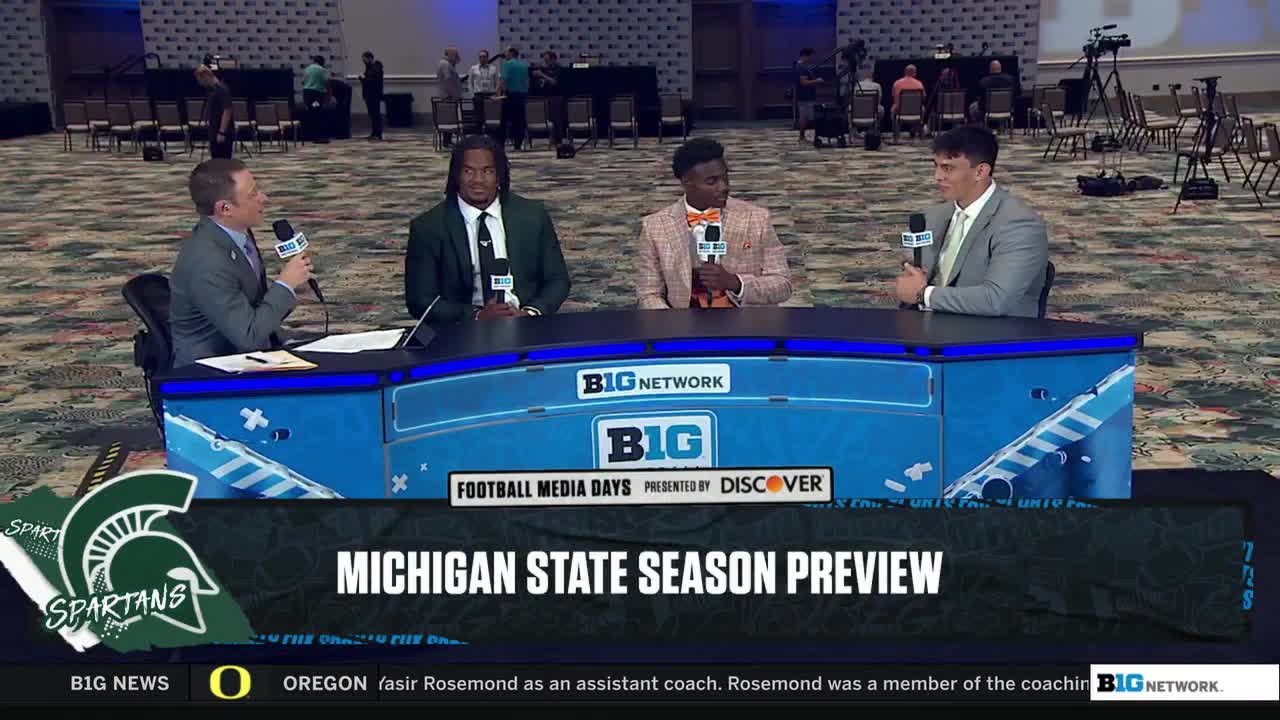 Four men sit behind a blue desk, each holding a microphone. The Big Ten Network logo is visible, and the graphic announces a Michigan State season preview.

