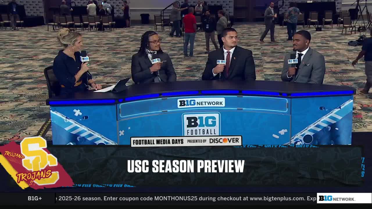 Four people in suits are seated behind a desk, each holding a microphone, ready to discuss the USC Trojans. The Big Ten Network logo is prominently displayed on the desk.
