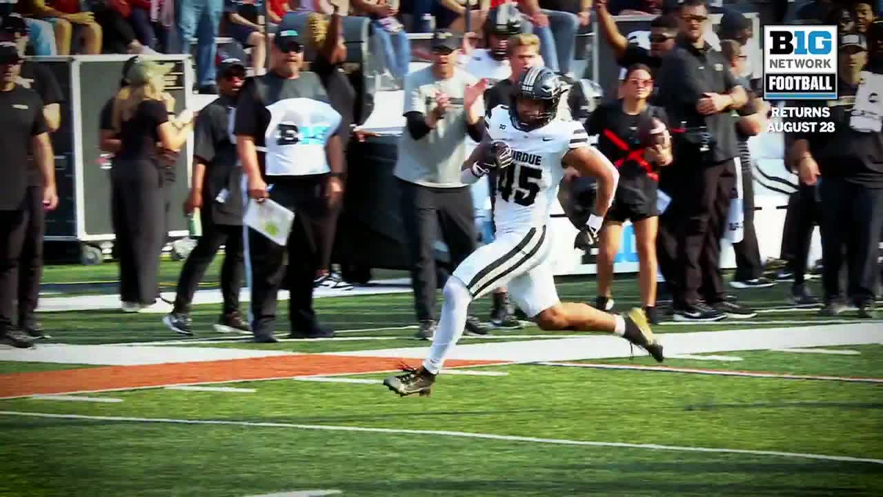 Number 45, in a Purdue uniform, sprints down the field, the football tucked securely in his left arm. The Big Ten Network logo is visible as the player gains ground, with a crowd of people watching from the sidelines.
