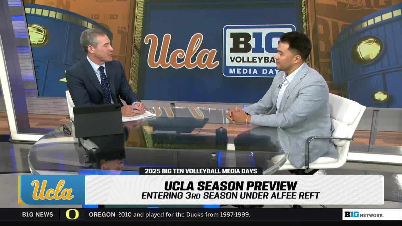 Two men sit at a table on a Big Ten Network set, engaged in a conversation. The backdrop displays "UCLA" and "Big Ten Volleyball Media Day" graphics.
