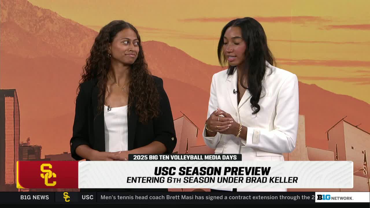 Two women are seated at a desk, speaking to the camera during a broadcast for the Big Ten Network. The woman in the white blazer gestures with her hands while the other looks on.
