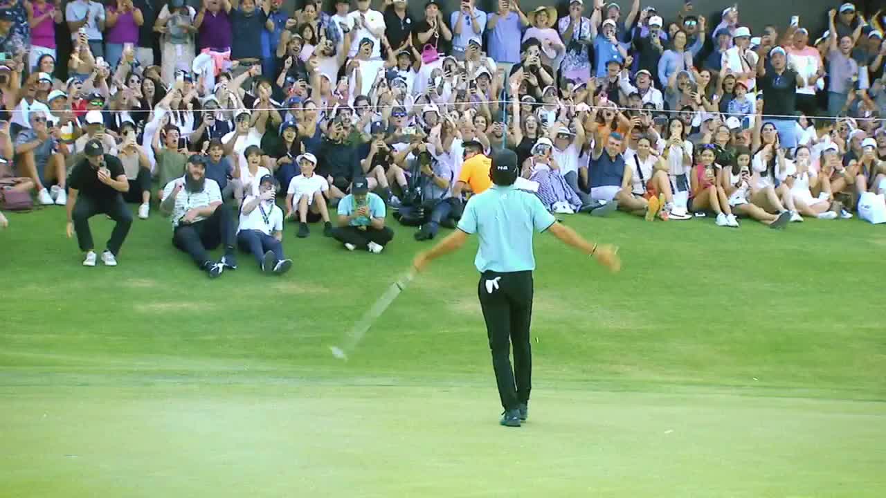 The golfer, arms outstretched, strides away from the green, the club still arcing through the air. A roaring crowd, their faces illuminated by the setting sun, celebrates behind him.
