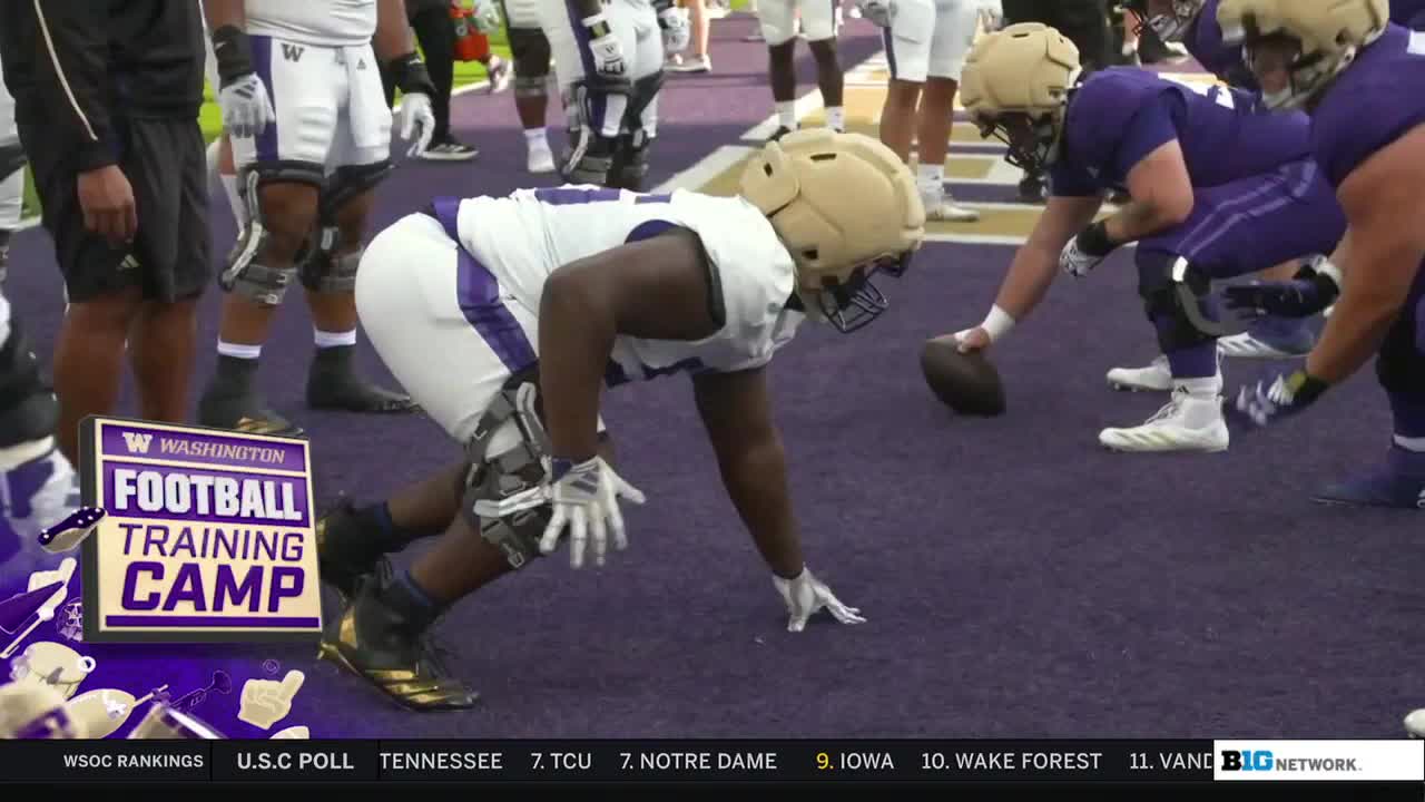 The Washington Huskies are in a three-point stance, ready to snap the ball. A player in a gold helmet and white jersey is focused, his hands on the ground.
