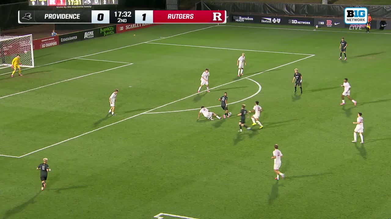 A player in black is on the ground, and the ball is nearby. White-clad players from Rutgers and others in black are converging on the ball.
