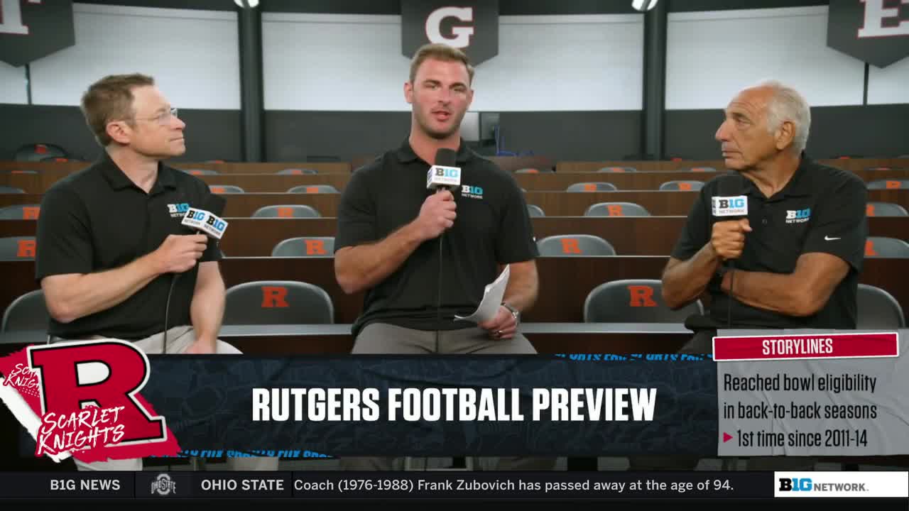 Three men in black shirts sit in a row, each holding a microphone with the Big Ten Network logo. The center man speaks into his mic, while the other two listen intently.
