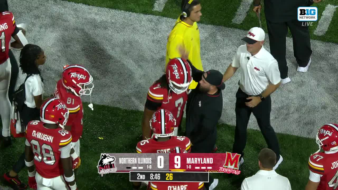 A Maryland player in a red helmet is being consoled by a man in a black cap, while the coach walks toward them. The scoreboard on the Big Ten Network shows Maryland leading Northern Illinois.
