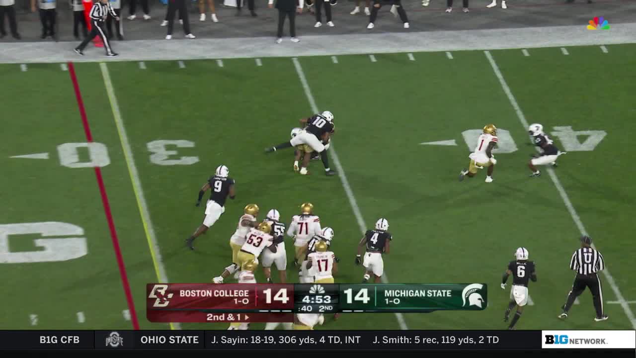 A Boston College player in white is being tackled by a Michigan State player wearing black. The play is near the 30-yard line, and the score is tied.
