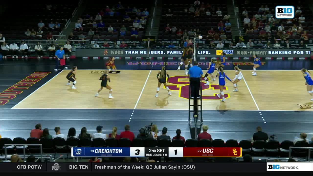 The ball hangs in the air as a player in black prepares to spike it. Across the net, the USC team in blue is poised to defend.
