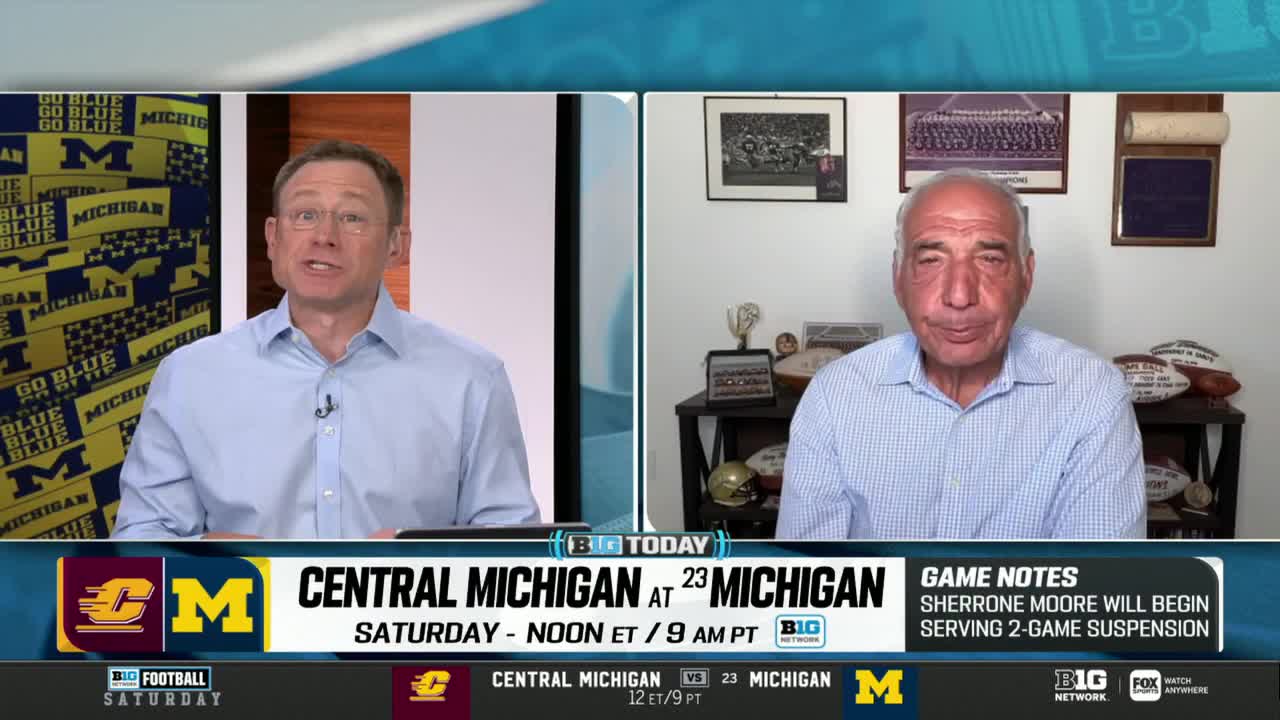 Two men in button-down shirts are on the Big Ten Network, discussing a football game between Central Michigan and Michigan. The broadcast's graphics include team logos and notes about a player's suspension.
