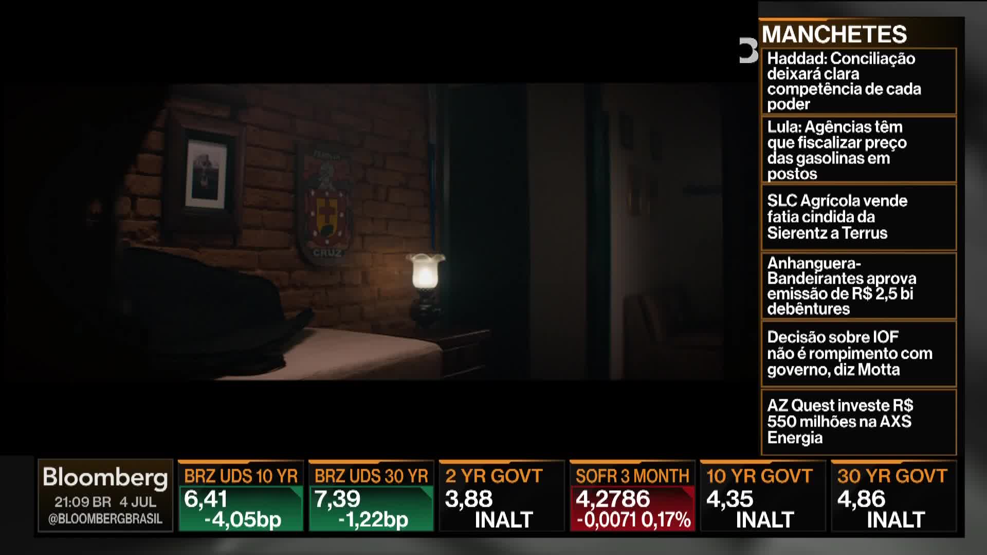 A Bloomberg TV screen displays financial data over a dimly lit room. On the right, news headlines scroll, while the bottom shows bond yields.
