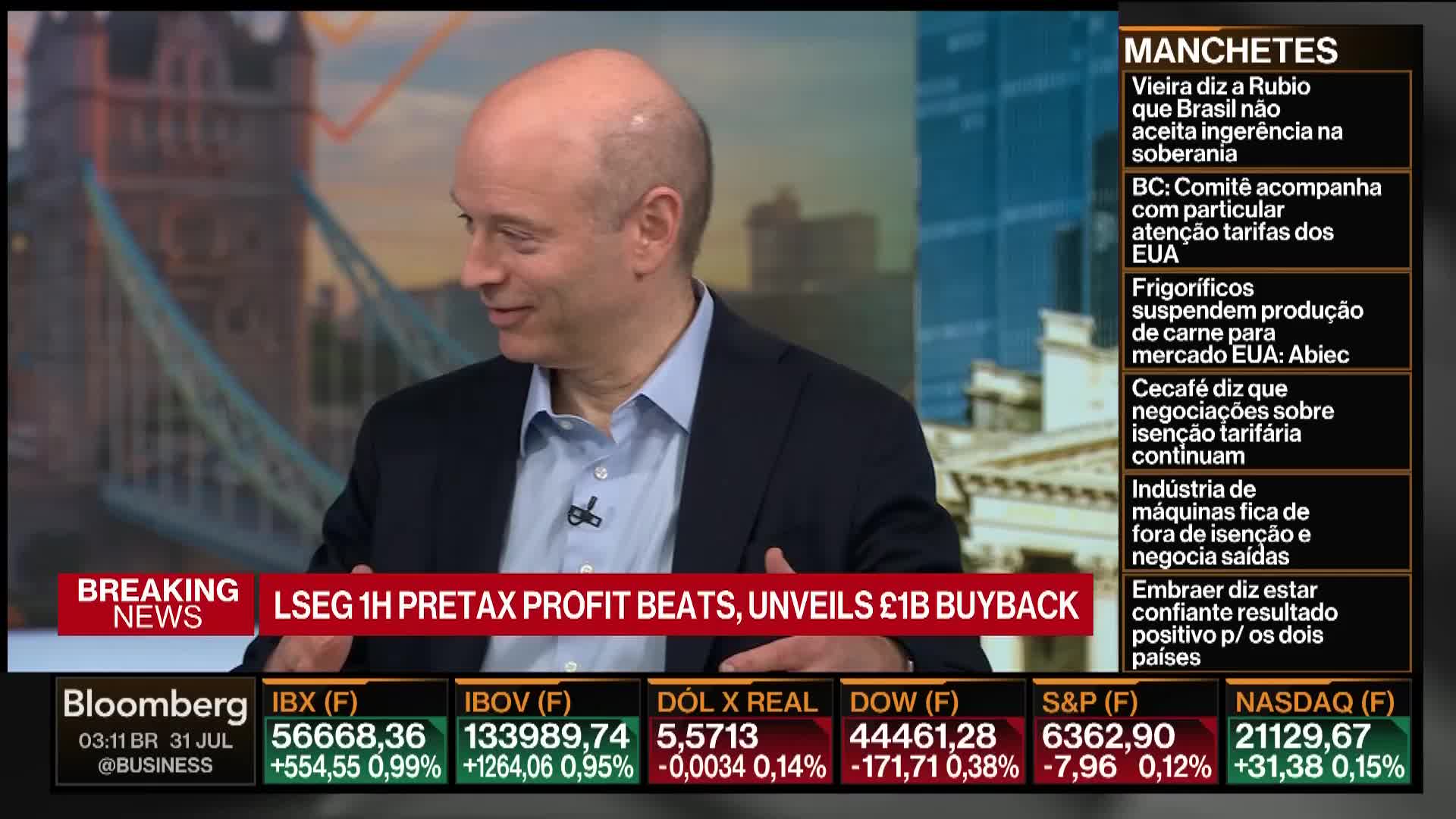 A man in a dark suit and light blue shirt smiles, speaking on Bloomberg TV. Below, the screen displays financial news and market data, including the NASDAQ and S&P.
