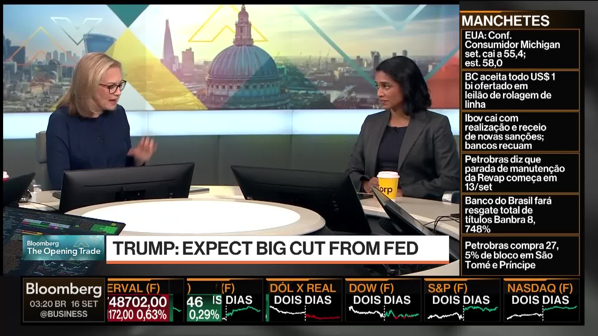On Bloomberg TV, two women sit at a desk, discussing the United States' economic policy. The woman on the left gestures with her hands while the other listens, a coffee cup in front of her.
