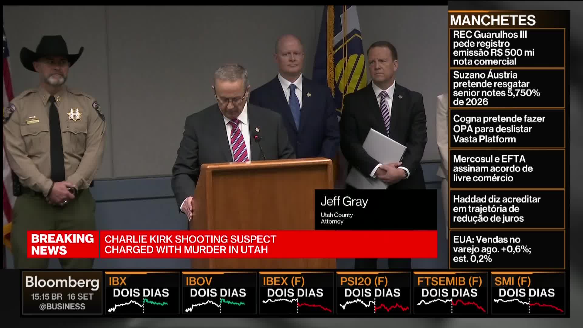 A man in a suit, identified as the Utah County Attorney, speaks from behind a podium. Behind him, two men in suits and a sheriff in uniform stand at attention.
The Bloomberg TV graphic displays breaking news about a shooting suspect charged with murder in Utah.
