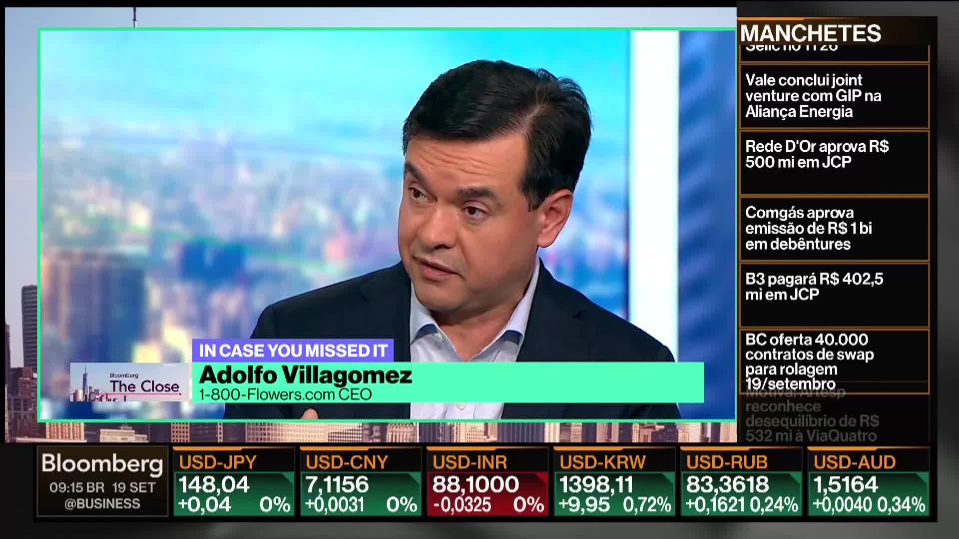 Adolfo Villagomez, the CEO of 1-800-Flowers, is speaking on Bloomberg TV. The screen displays financial news headlines and currency exchange rates below him.
