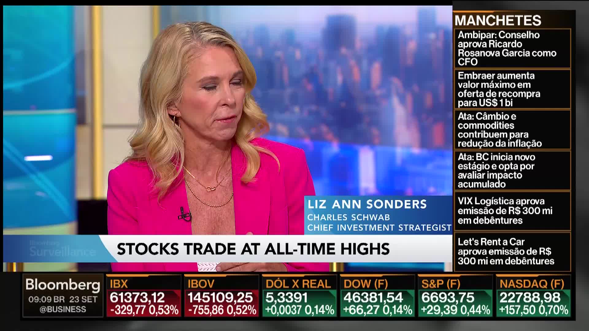 A woman in a bright pink blazer is speaking on Bloomberg TV, with the words "Stocks Trade at All-Time Highs" displayed below her. The screen also shows stock market data and headlines in Portuguese.
