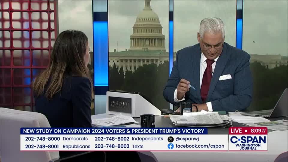 A man in a suit, seated at a desk, holds a pen and looks down at papers. The C-SPAN logo is visible, and the U.S. Capitol building is in the background.
