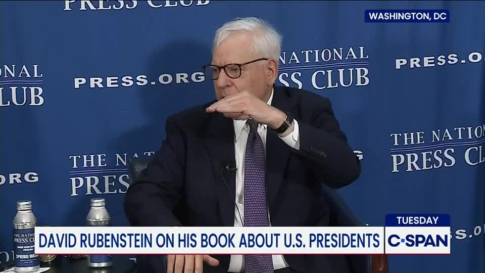 David Rubenstein, in a suit and tie, gestures with his hand at the National Press Club. The C-SPAN logo is visible along with a banner noting he's discussing his book about U.S. presidents.
