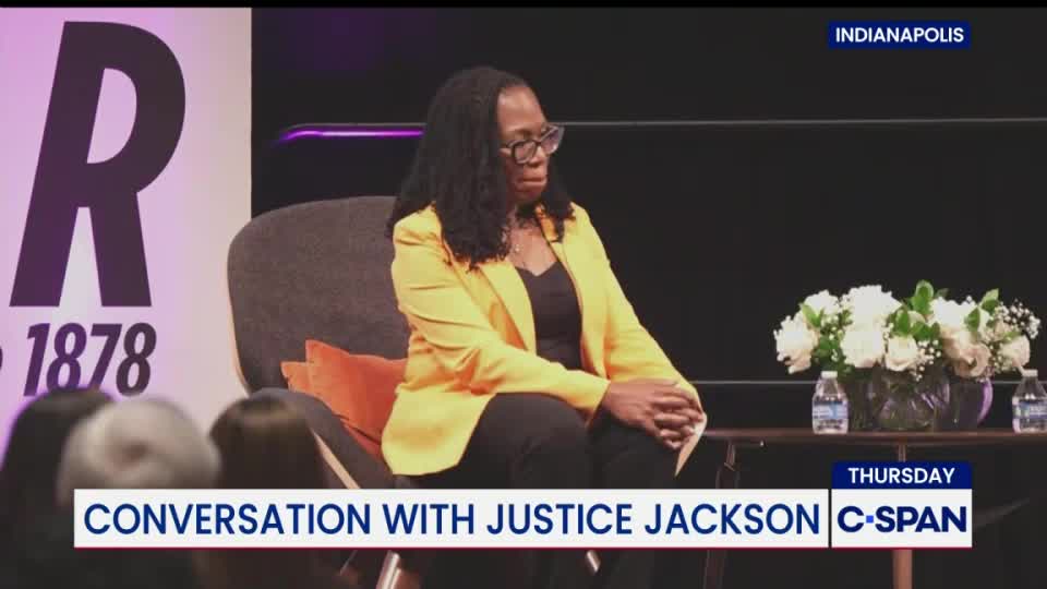 Justice Jackson, in a yellow blazer, sits on a chair, her hands clasped in her lap. The C-SPAN logo is visible as she appears to be participating in a conversation in Indianapolis.
