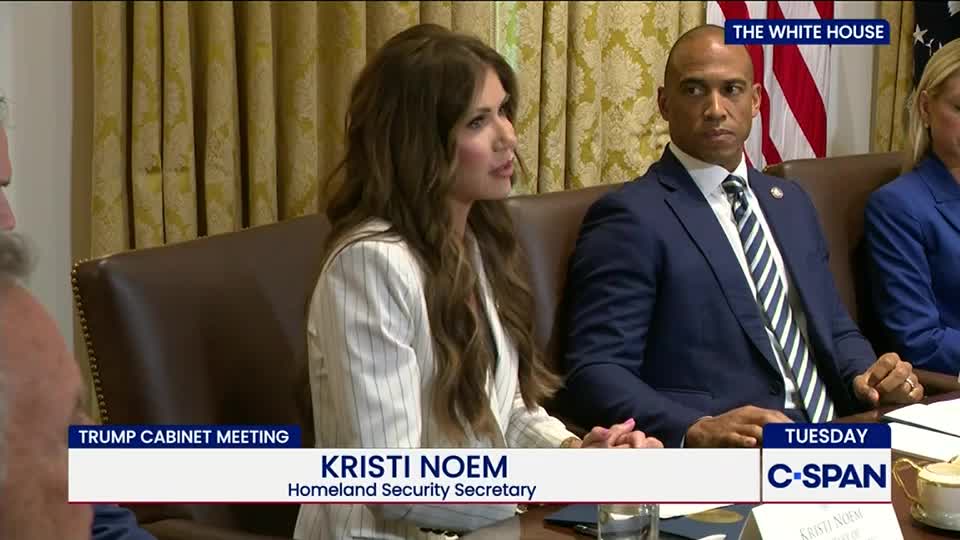 Kristi Noem, identified as Homeland Security Secretary, speaks at a table during a Trump Cabinet meeting, as captured by C-SPAN. A man in a dark suit sits to her right, listening intently.
