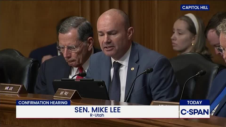 Senator Mike Lee is speaking, his gaze fixed on a tablet.  A man to his left, wearing glasses, looks down, while the C-SPAN logo and "Confirmation Hearing" are displayed on the screen.
