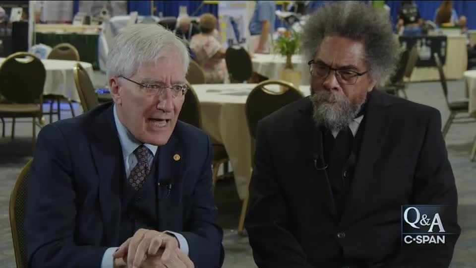 A man in a dark suit and tie gestures emphatically as he speaks, while the other man, wearing a black suit, listens intently. The C-SPAN logo is visible in the corner.
