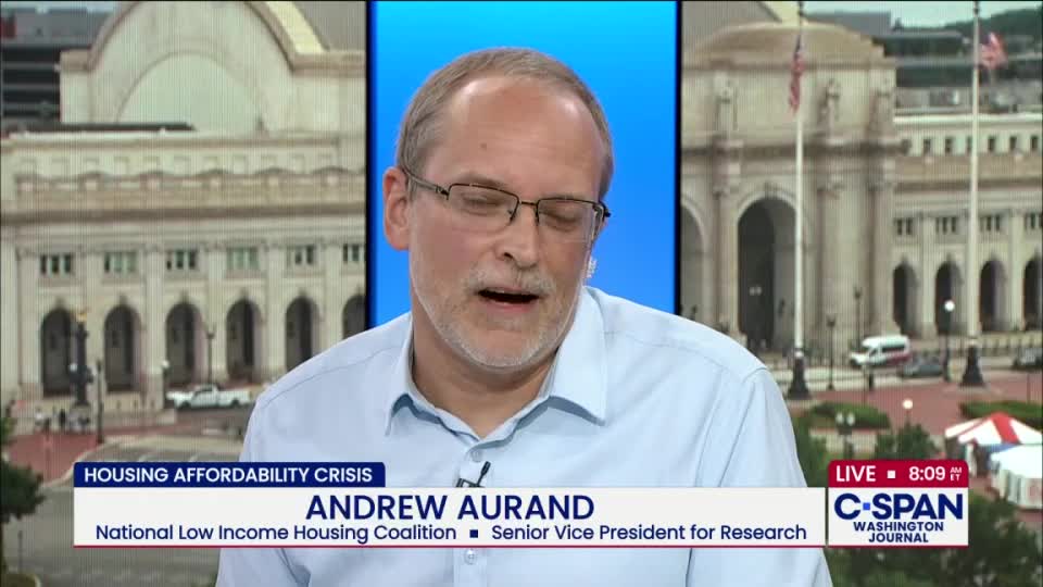 A man wearing glasses and a light blue shirt speaks on C-SPAN, the background showing a building in Washington, D.C. The lower third of the screen identifies him as Andrew Aurand, discussing the housing affordability crisis.
