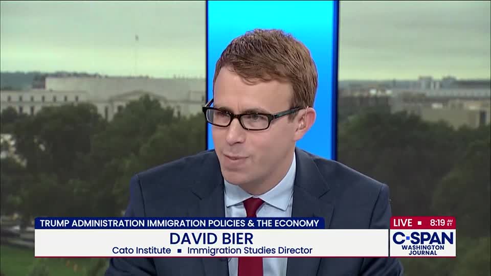 A man in a suit and glasses is speaking on C-SPAN's "Washington Journal," discussing immigration policies. The backdrop shows a view of a building in Washington, D.C.
