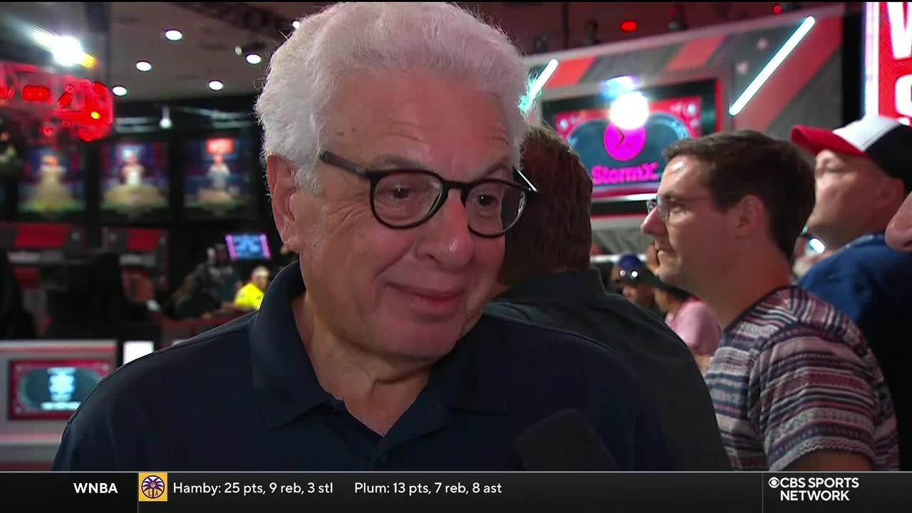 A man with glasses smiles into a microphone, likely being interviewed on CBS Sports Network USA. Behind him, a crowd of people watches a screen with the StormX logo.
