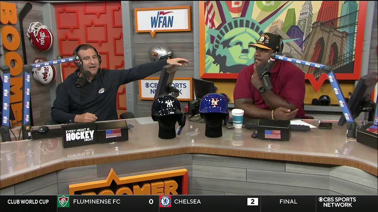 The man on the left gestures toward three hats, each on a mannequin head, while the other man listens intently. A CBS Sports Network USA logo is visible on the screen below.
