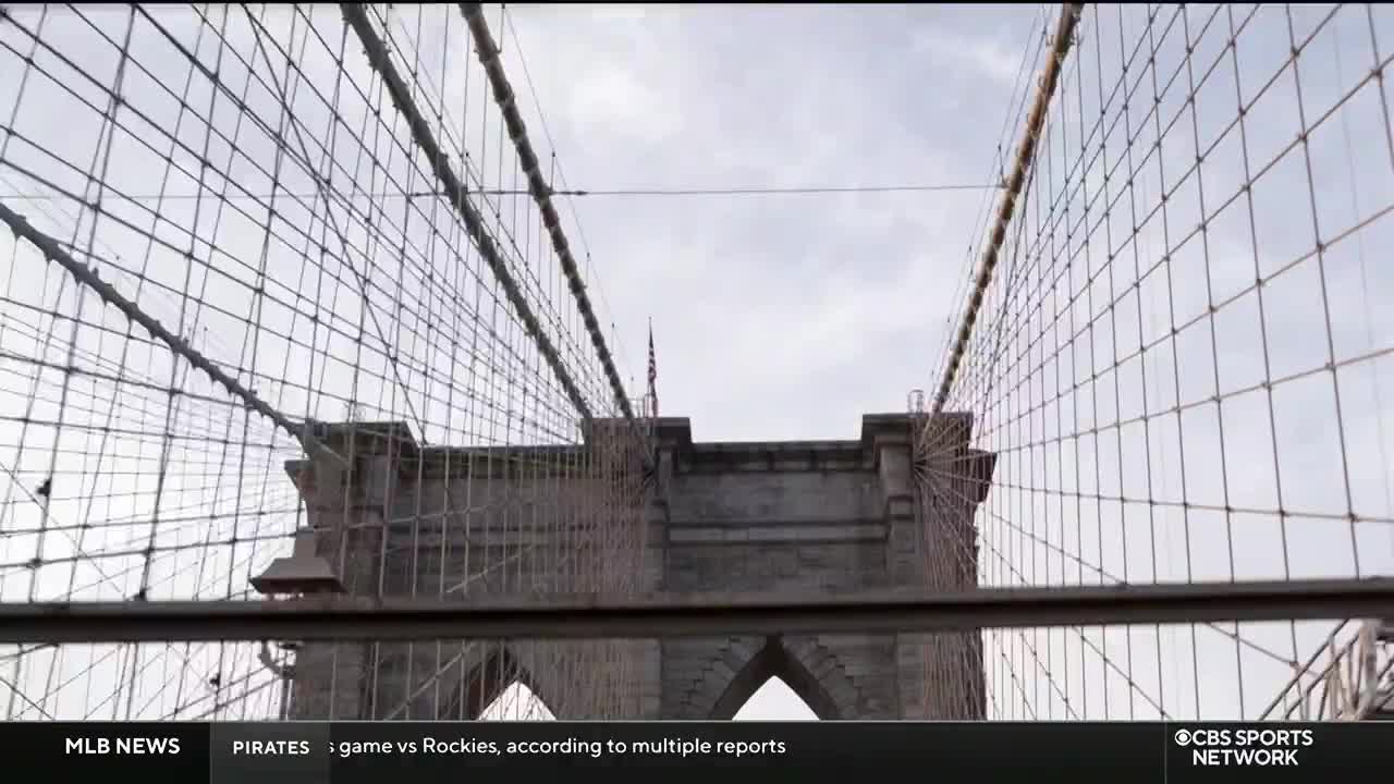 The camera angle frames the Brooklyn Bridge's intricate web of cables and stone towers, highlighted against a cloudy sky.  CBS Sports Network USA's logo is visible at the bottom right.
