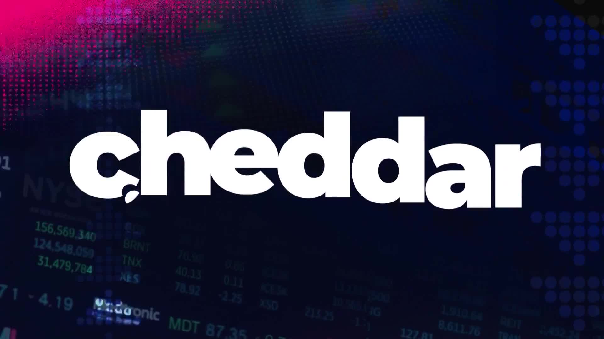 The word "cheddar" in bold white letters dominates the screen. Behind it, a dark blue background displays stock market data and a splash of pink and purple light.
