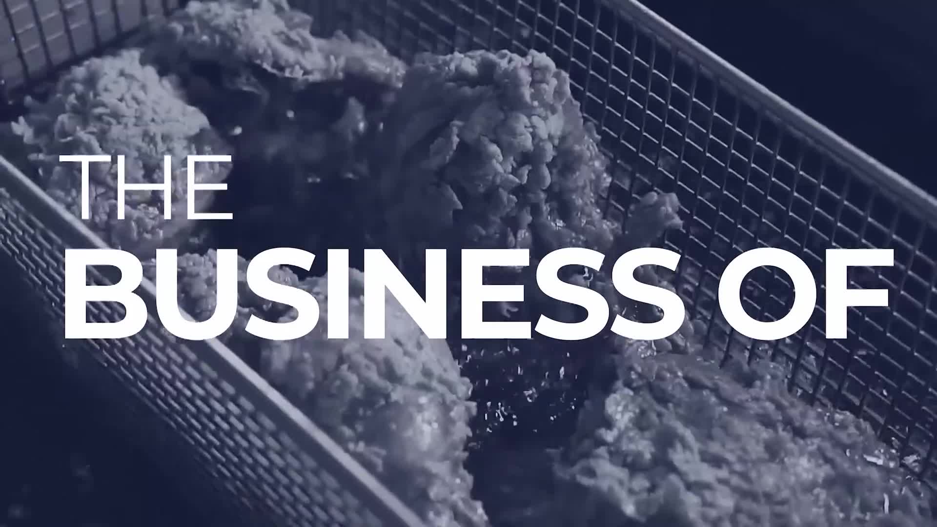 Crispy, golden-brown fried chicken pieces sit in a metal basket, submerged in hot oil. The scene suggests a segment on Cheddar News about the food industry in the United States.
