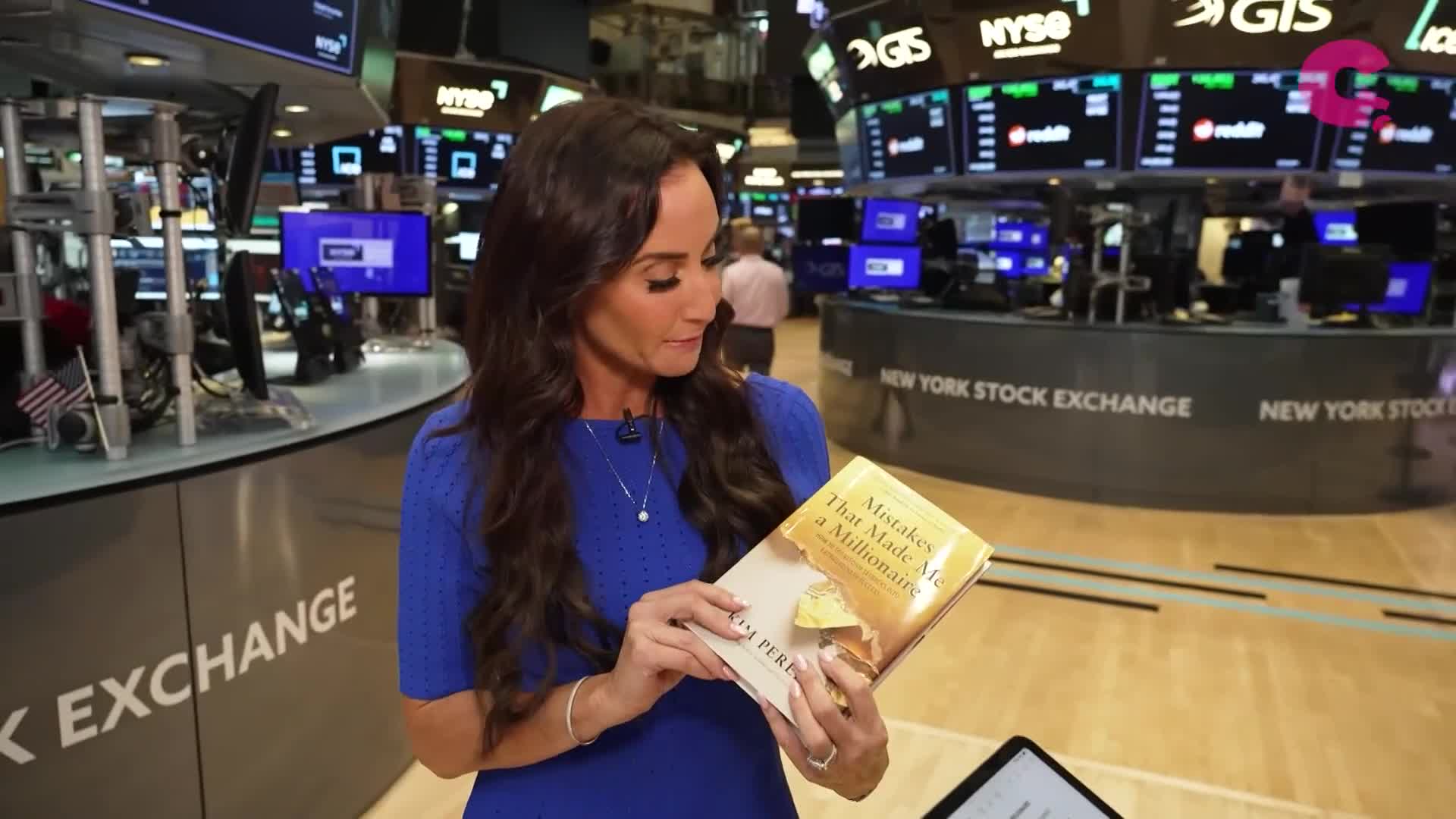 Standing on the floor of the New York Stock Exchange, a woman in a blue dress holds a book titled "Mistakes That Made Me a Millionaire." Behind her, screens display financial data, and the NYSE logo is visible.
