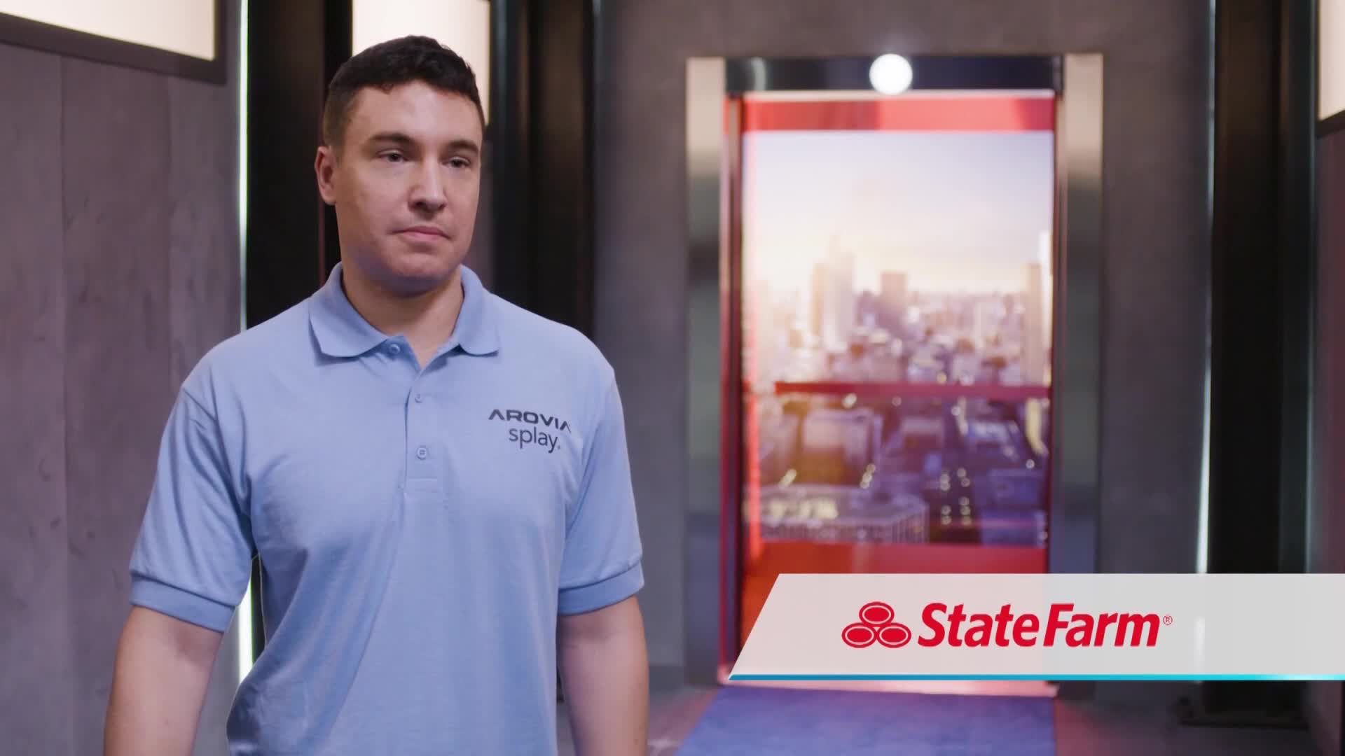 A man in a light blue polo shirt walks toward the camera, his expression neutral. Behind him, a window looks out onto a cityscape, and a State Farm logo is displayed in the bottom right corner.
